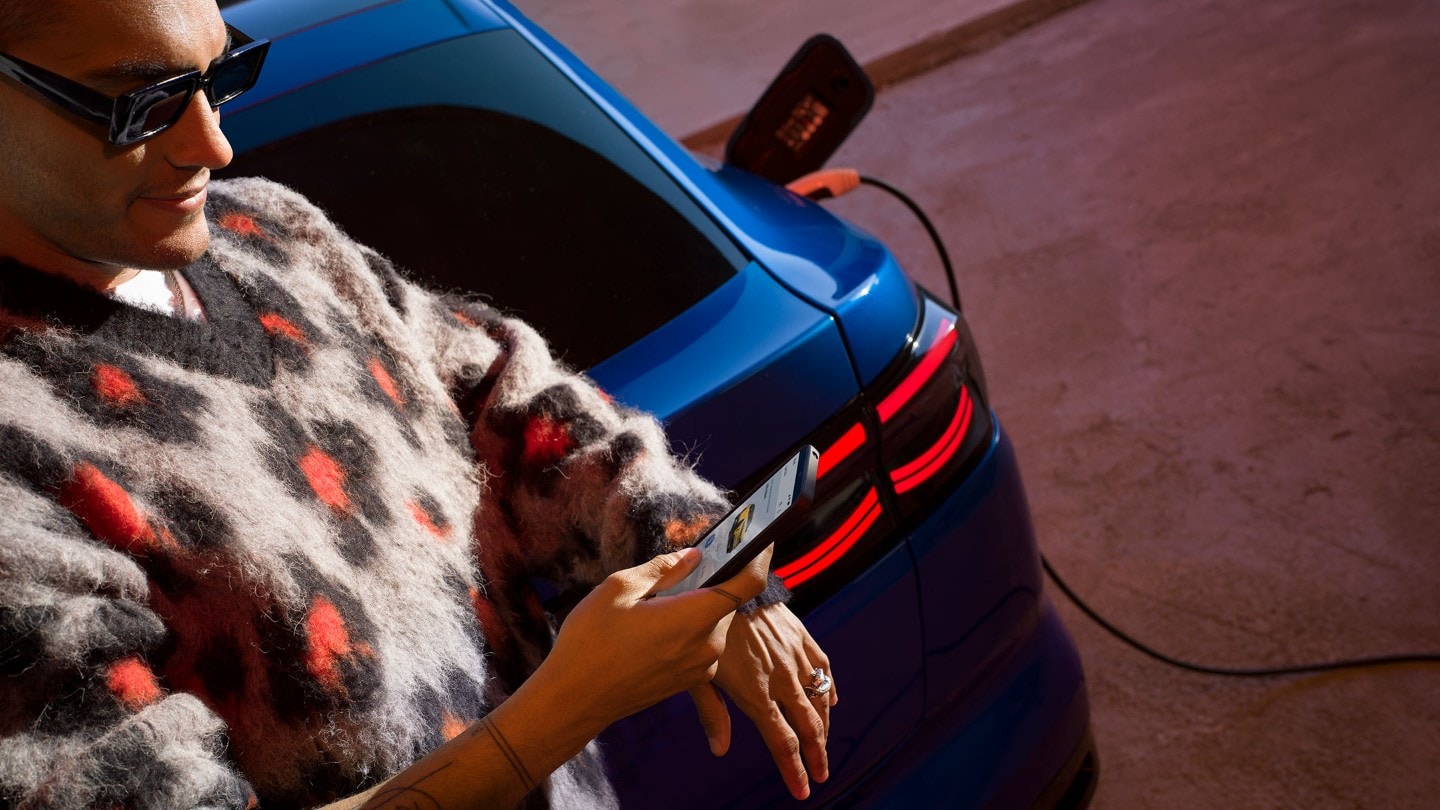 A man looks at his phone while leaning on the boot of a blue electric Ford Capri