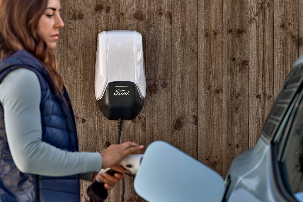 A woman plugs her blue Ford Explorer electric vehicle into a EV home charging point.