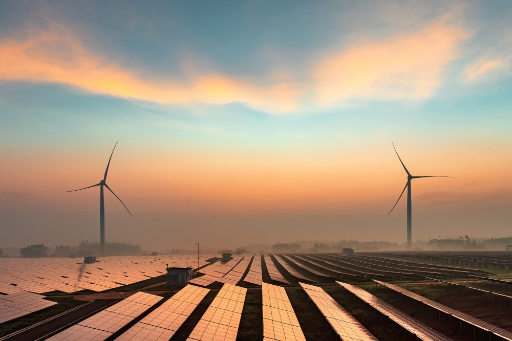 Renewable energy sources, including wind turbines and solar energy panels, shown at sunset. 