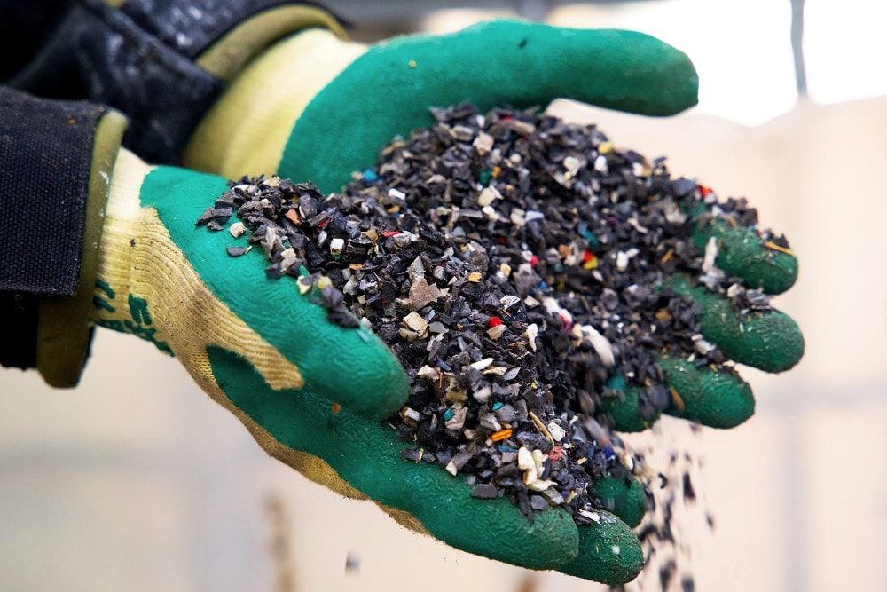 Hands wearing rubber gloves holding pieces of recycled plastic waste.