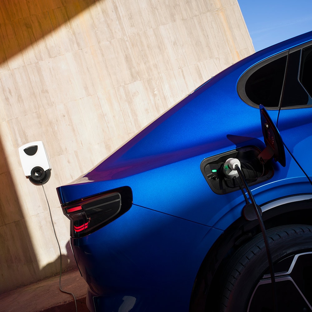 A  rear view of a blue Ford Capri eletric vehicle plugged in to an EV home charging point. 