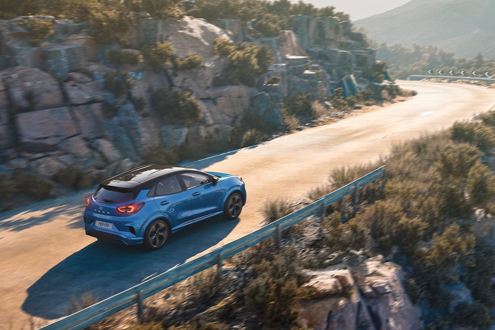 A blue Puma Gen-E driving along a winding mountain road.