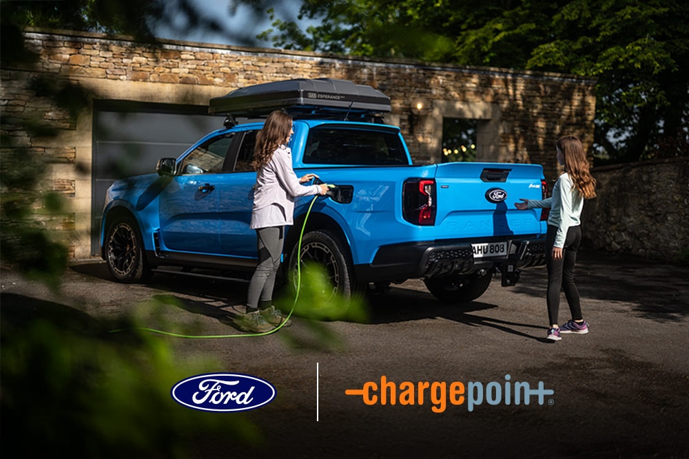 Two people charging a blue Ford pickup at a home garage. Ford and Chargepoint logos visible.
