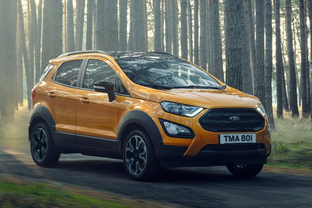 An orange Ford EcoSport SUV driving through a forest.
