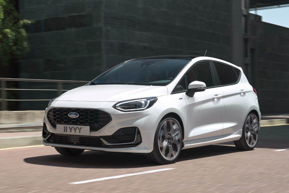A white Ford Fiesta hatchback driving on an urban road.