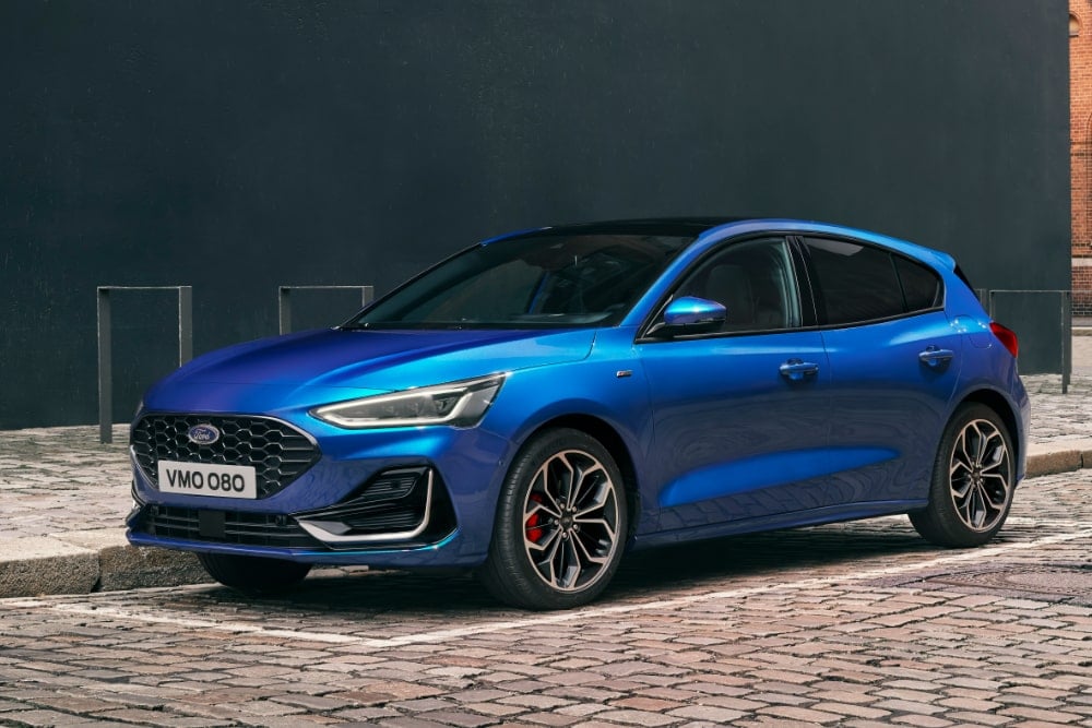 A blue Ford Focus hatchback parked on a cobbled city street.