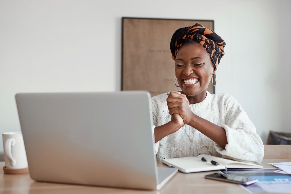 A person smiling and clenching their fists in front of a laptop, showing excitement.