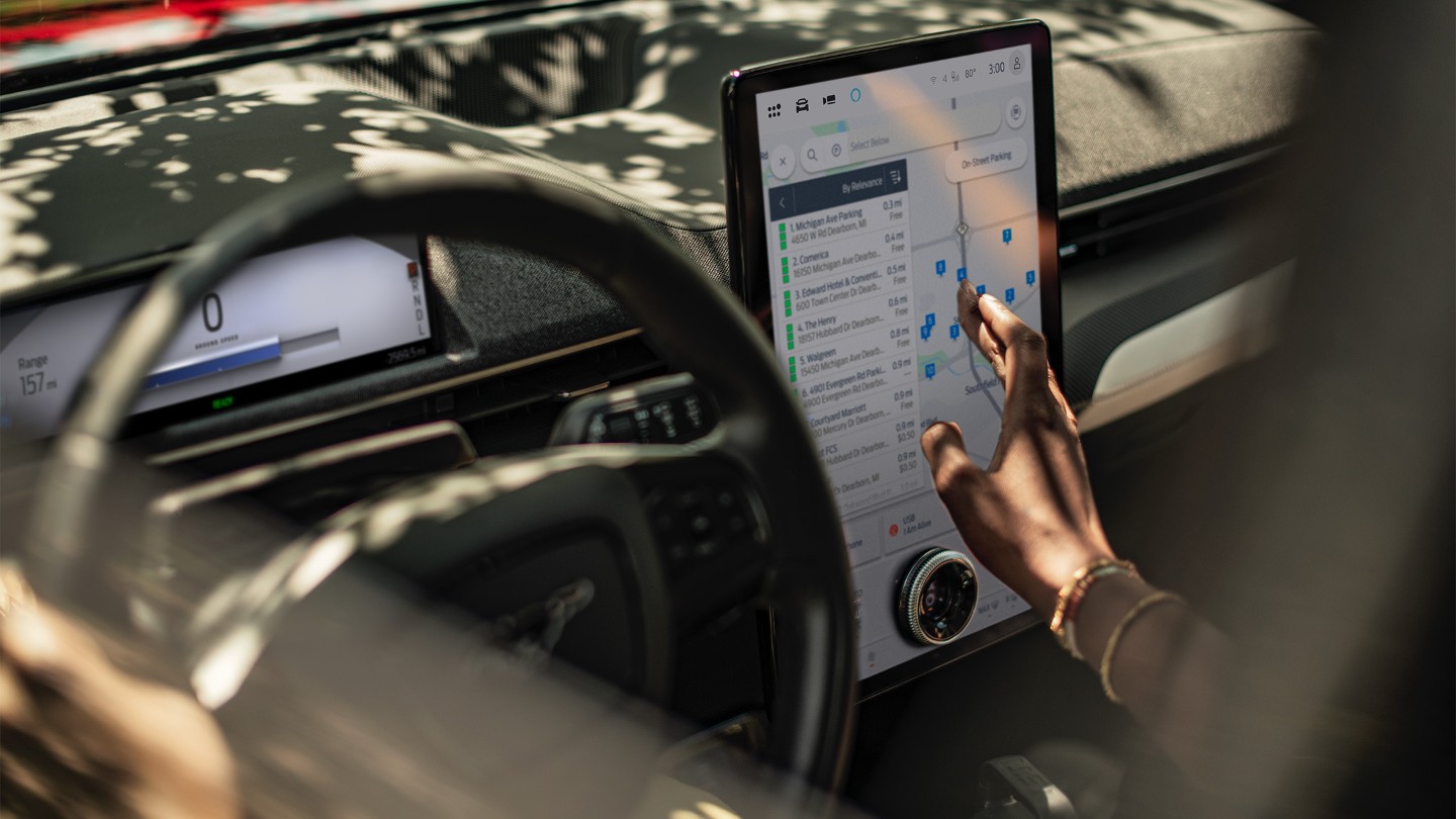 A close up of a woman in a Ford Mustang Mach-E interacting with the large SYNC touchscreen.