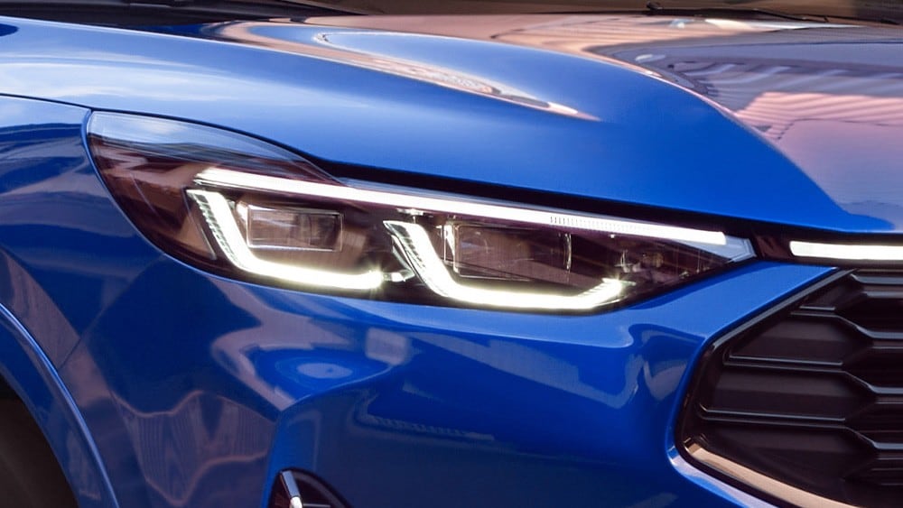 A close up of the front headlight of a blue Ford Mustang Mach-E.