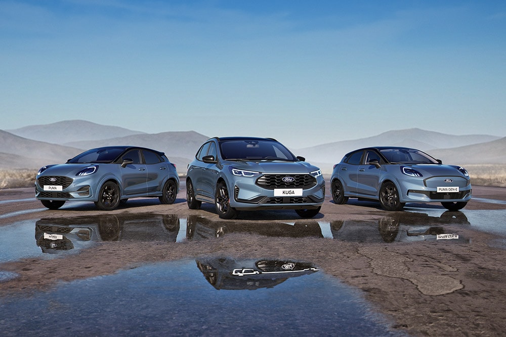 A Ford Puma, Ford Kuga, and Ford Puma Gen-E parked on a wet road with mountains in the background.