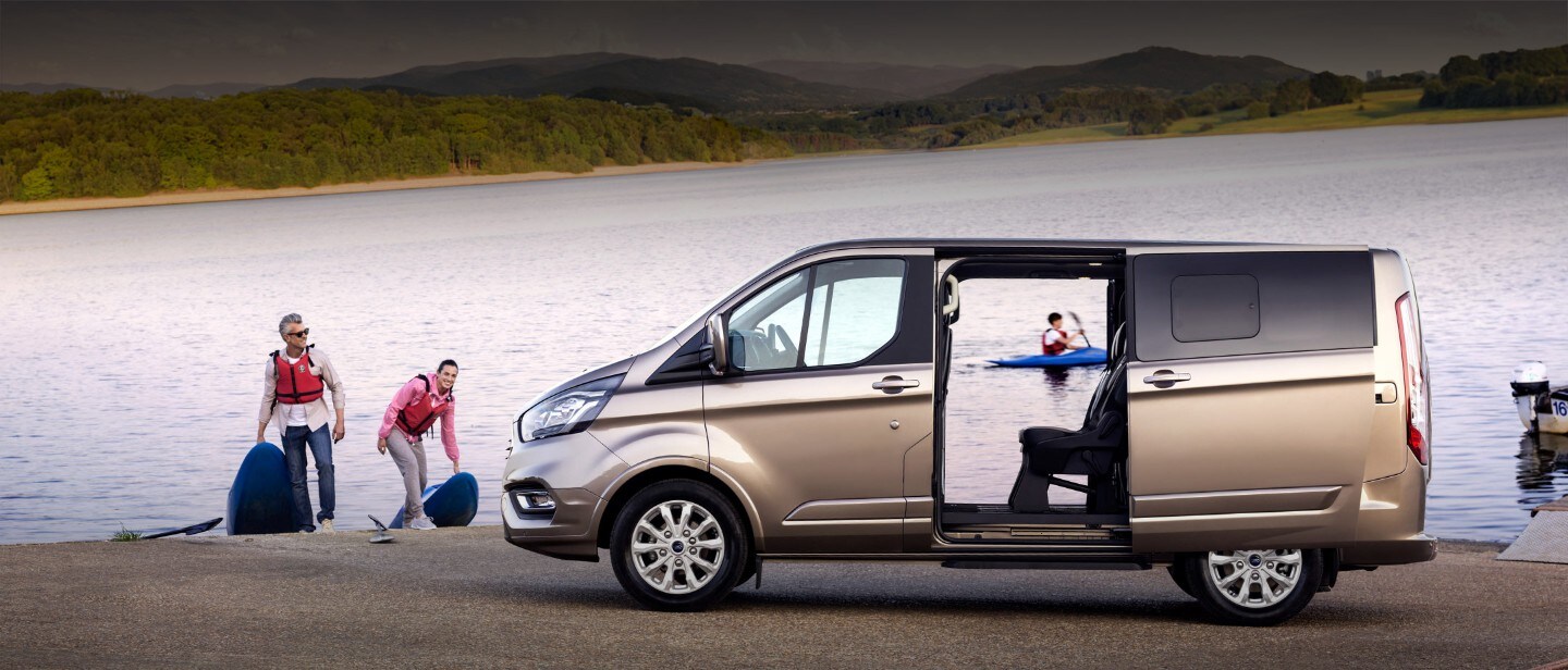 Grey Ford Tourneo Custom with wide open doors at water park and family canoeing