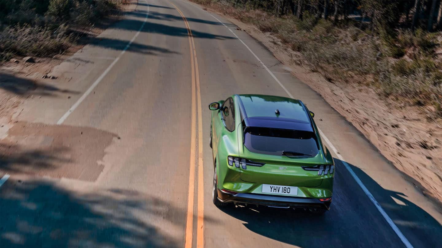 A Ford Mustang Mach-E GT in Eruption Green driving on a mountain road lined with trees.