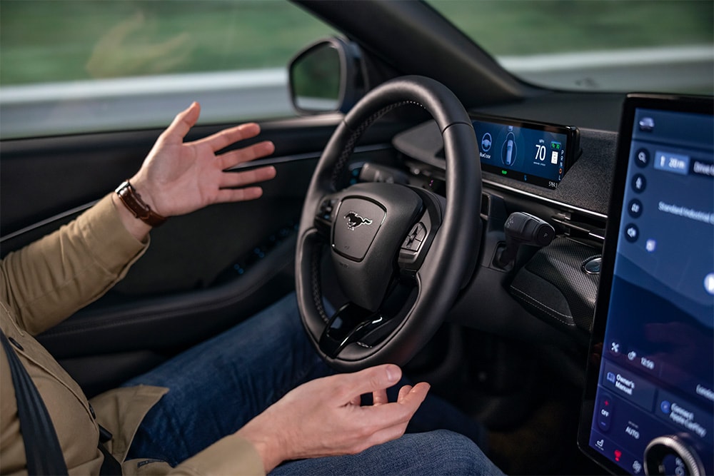 A pair of hands hover by the steering wheel of the Mustang Mach-E, demonstrating the BlueCruise autonomous driving technology