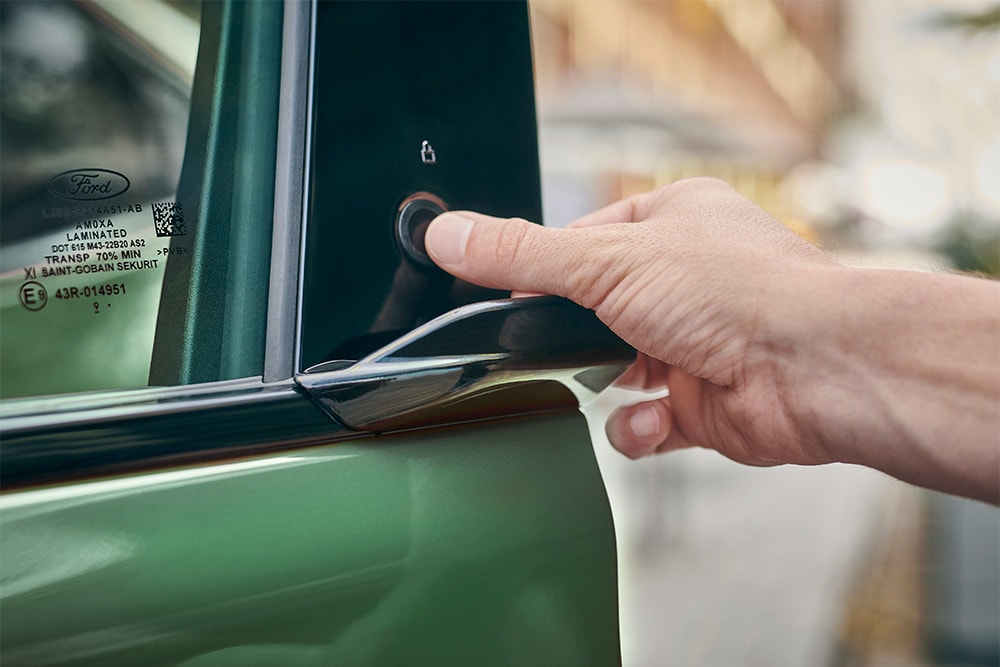 A close up of a hand operating the E-Latch system by pressing a button the door of a green Ford Mustang Mach-E.