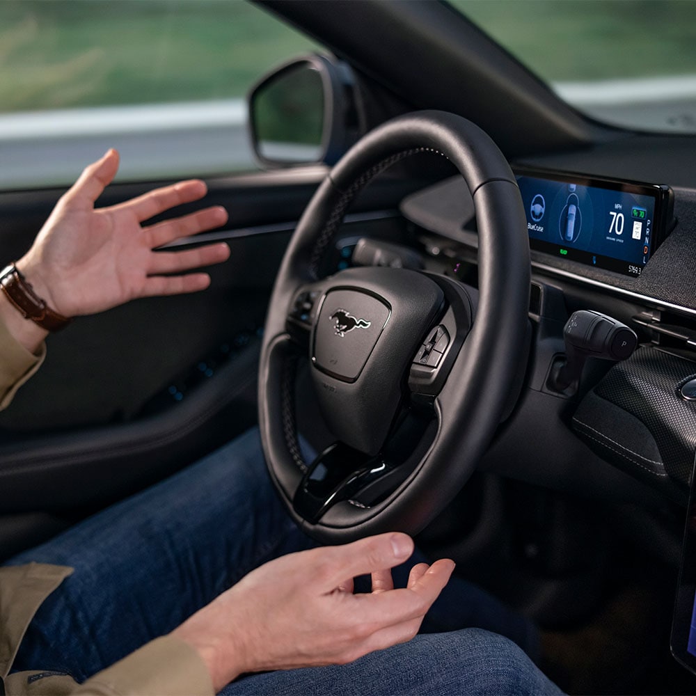 A pair of hands hover by the steering wheel of the Mustang Mach-E, demonstrating the BlueCruise autonomous driving technology