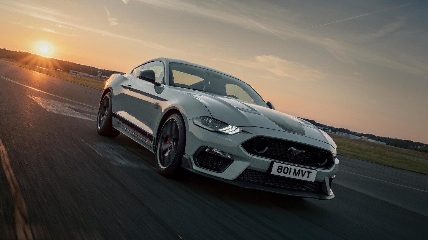 Ford Mustang Mach 1 drving on a racetrack against a sunset backdrop