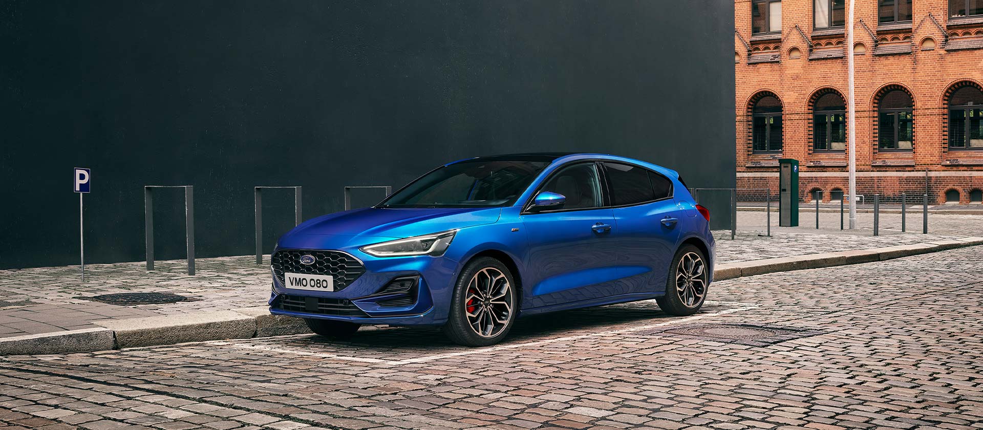 A blue Ford Focus hatchback parked on a cobblestone street in an urban setting.