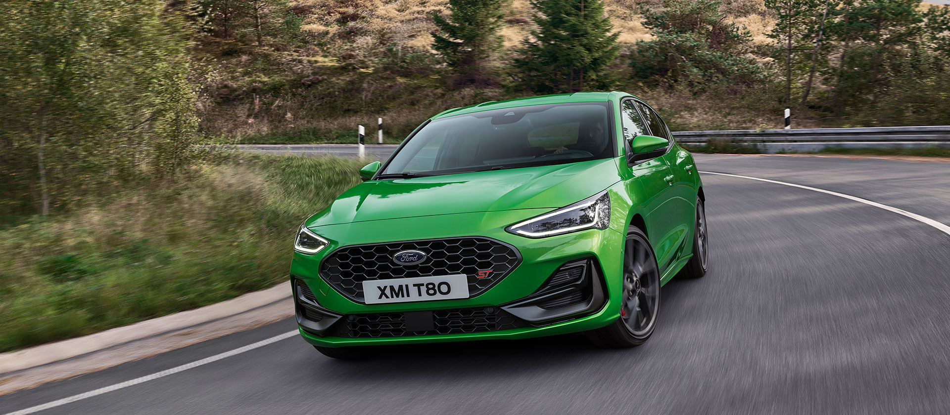 A Mean Green Ford Focus ST driving around a corner on a scenic road.