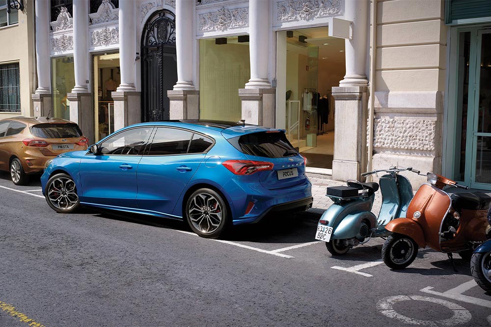 A blue Ford Focus manoeuvring into a city parking space using the Active Park Assist feature.