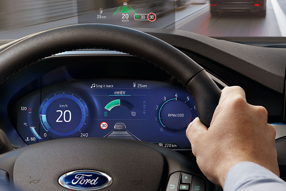 Hand holding a steering wheel with a small monitor above the dashboard