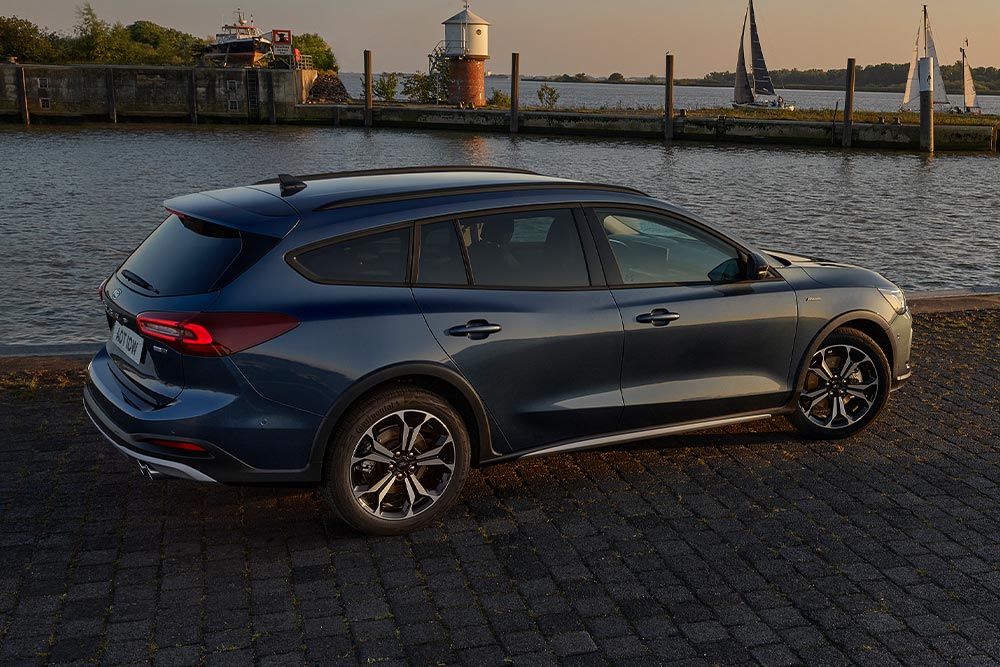 A dark blue Ford Focus Active Estate parked next to a body of water at dusk.