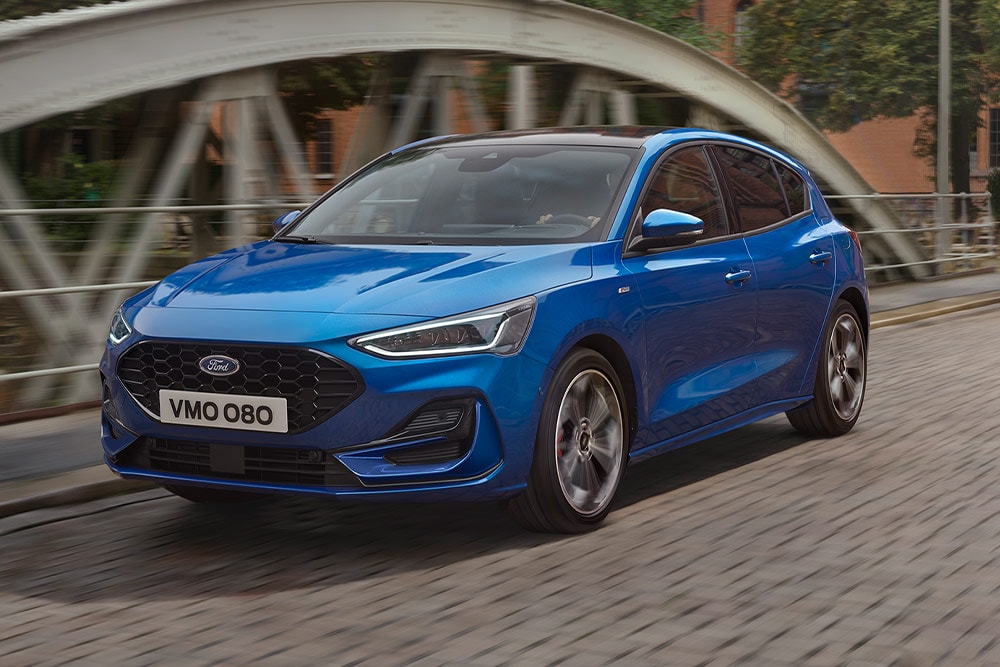 A blue Ford Focus hatchback driving over a bridge.