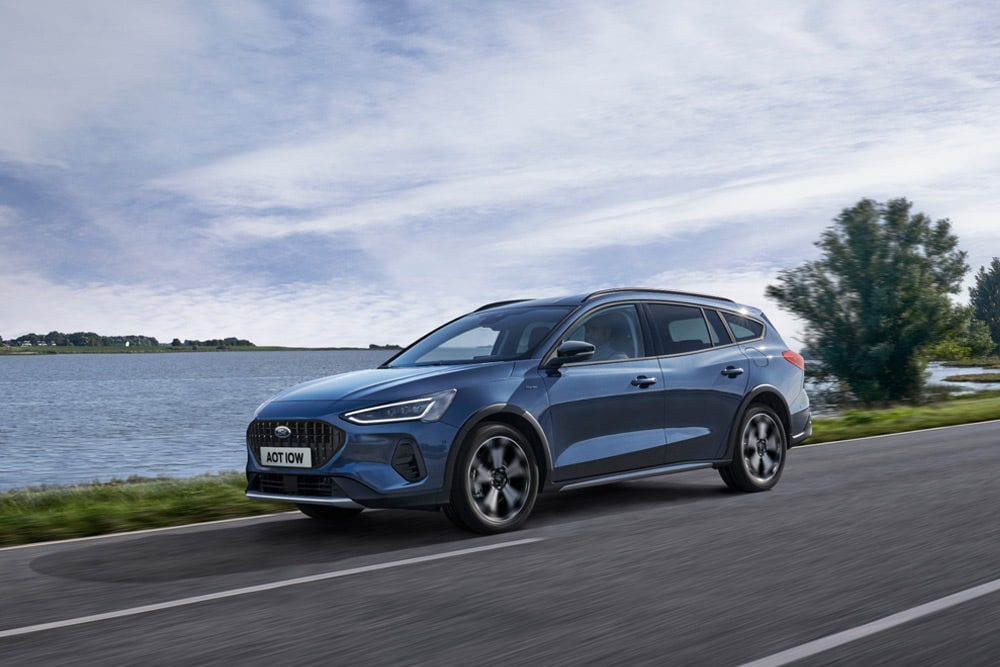 A blue Ford Focus estate/wagon is parked on a paved road next to a body of water. 