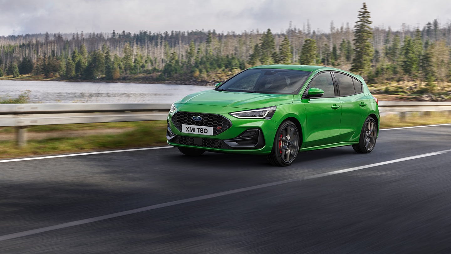 A Ford Focus ST in Mean Green driving on a road with trees in the background.