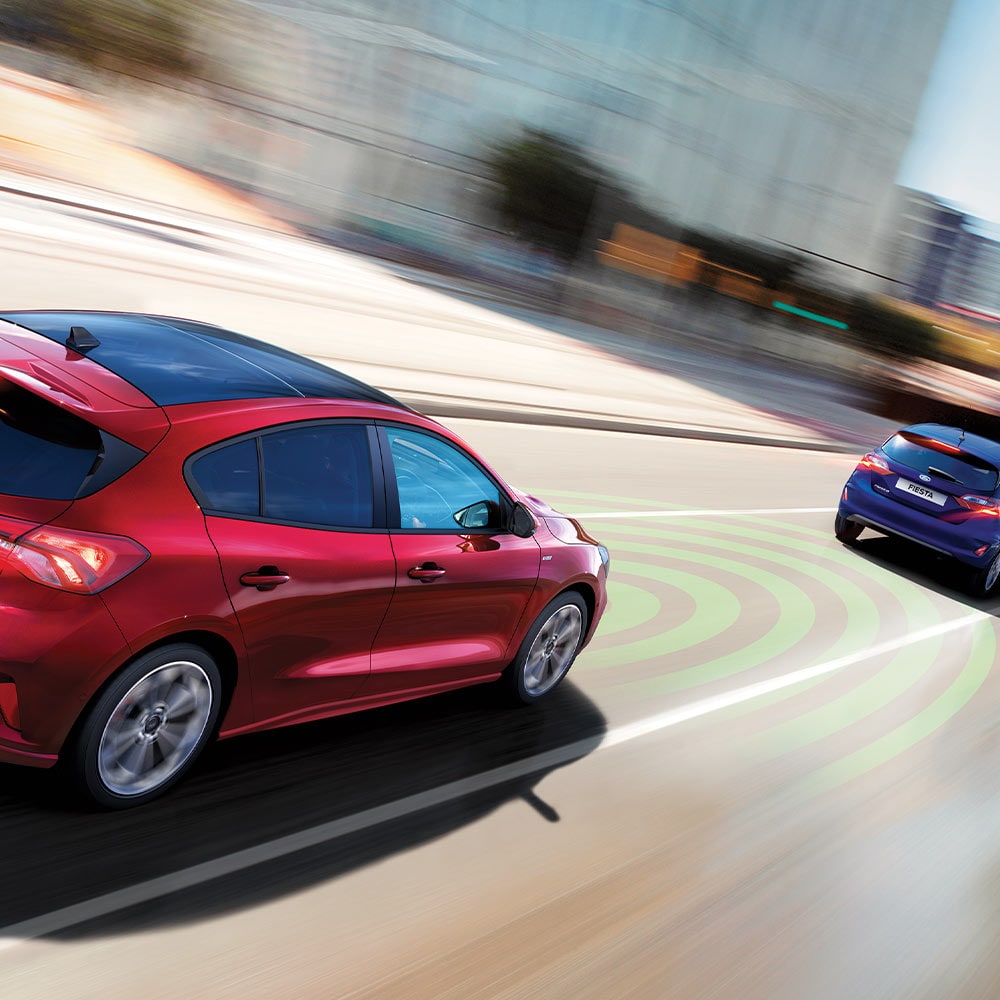 A graphic showing a red Ford Focus using sensors, indicated by blue lines, to detect the car in front as part of the Emergency Braking system.