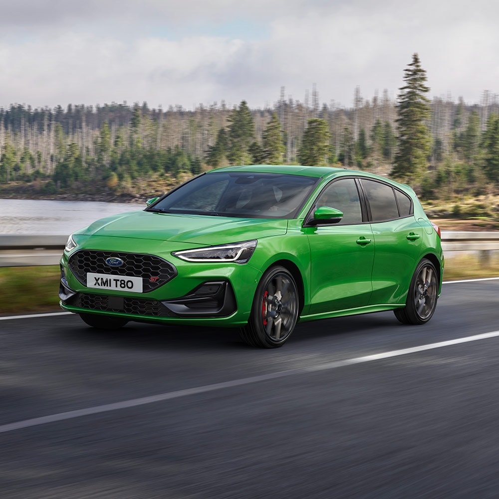 A Mean Green Ford Focus ST driving on a winding road surrounded by trees.