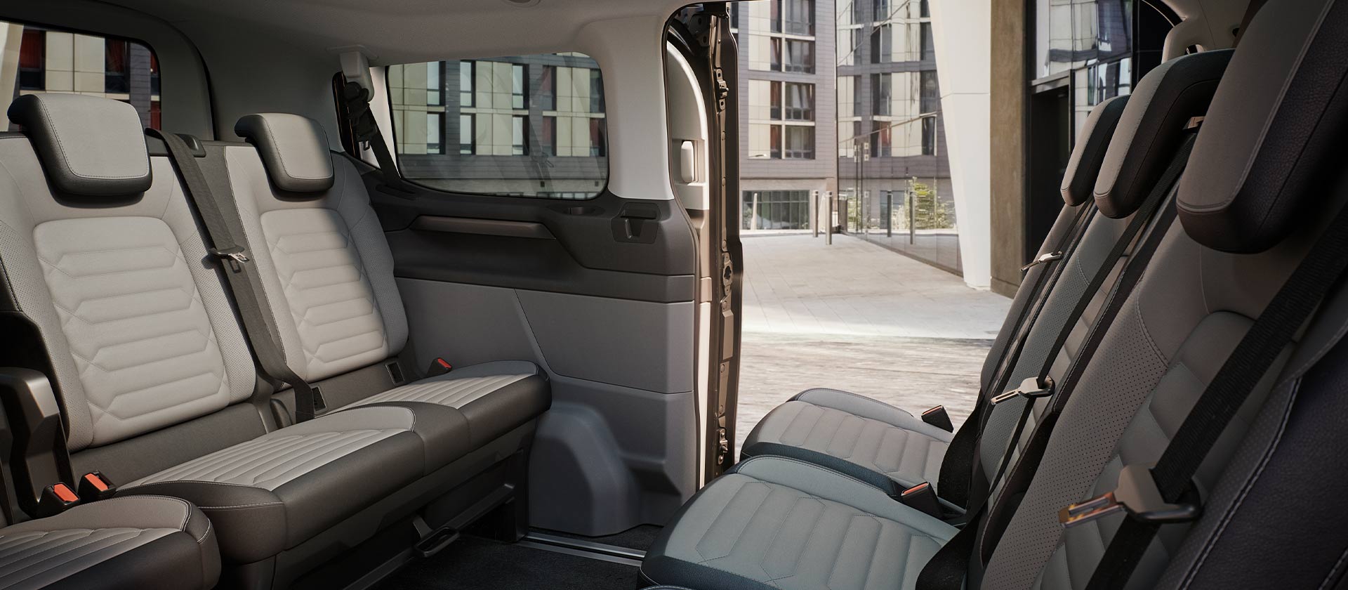Interior view of the Ford Tourneo Custom, showing multiple rows of grey passenger seats and panoramic sunroof.