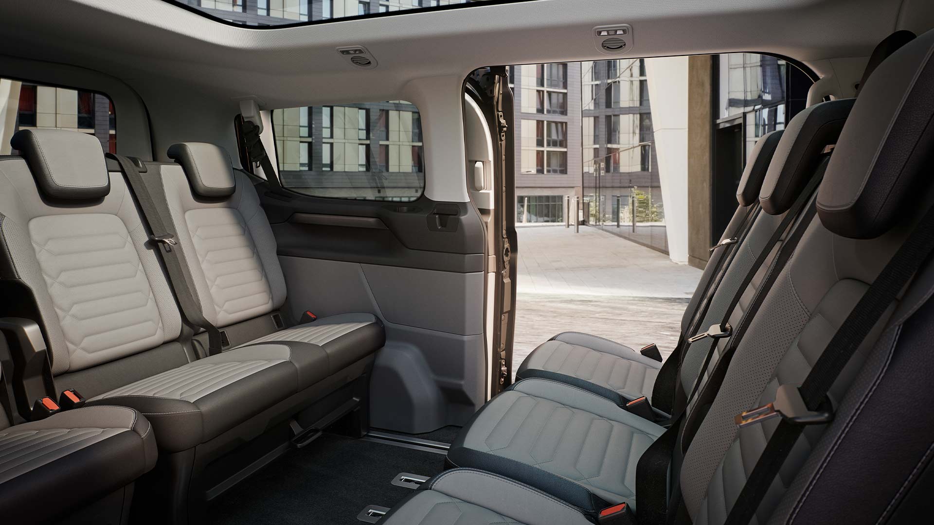 Interior view of the Ford Tourneo Custom, showing multiple rows of grey passenger seats and panormaic sunroof.
