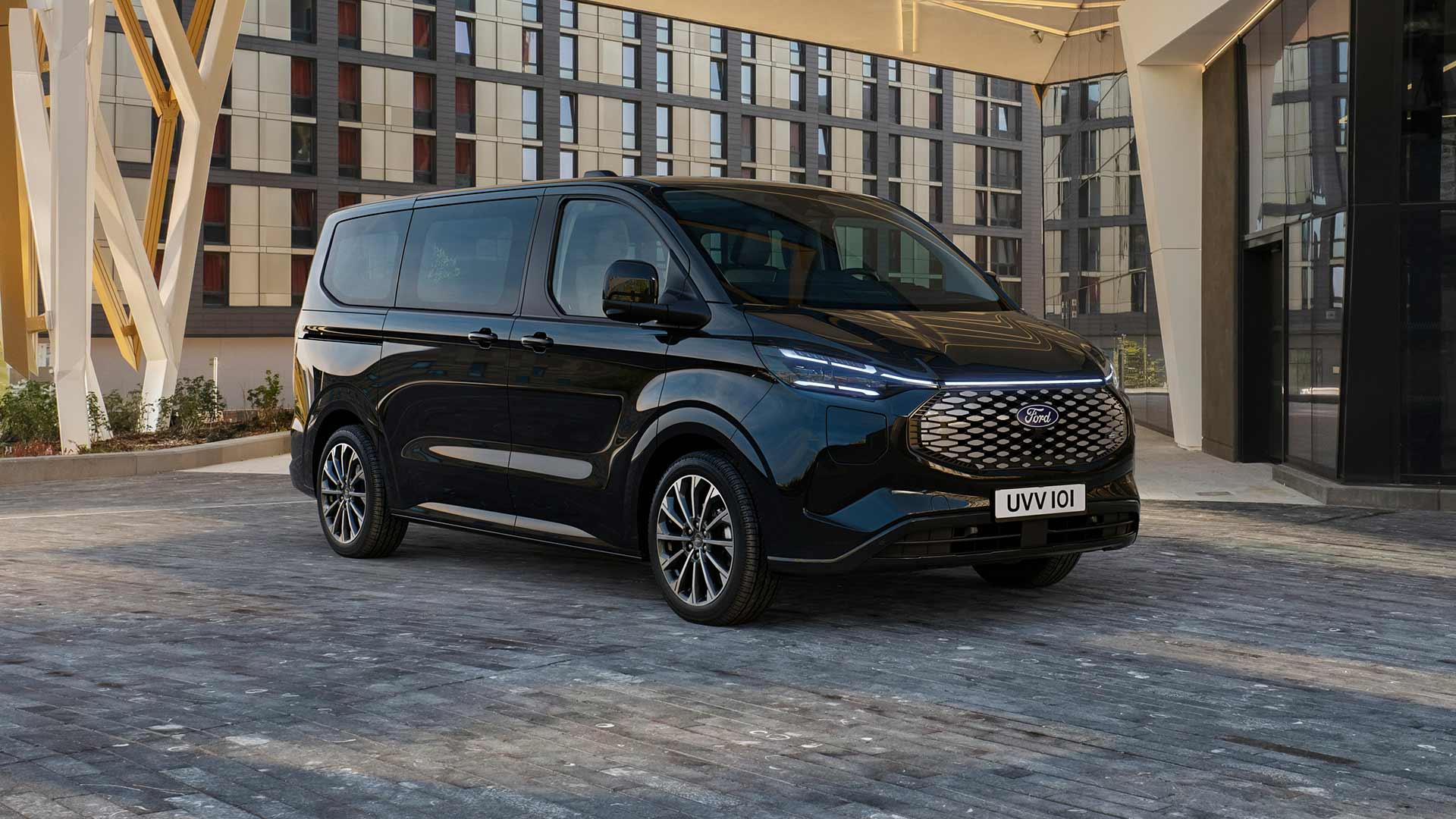 A black Ford E-Tourneo Custom is parked in front of a modern building.