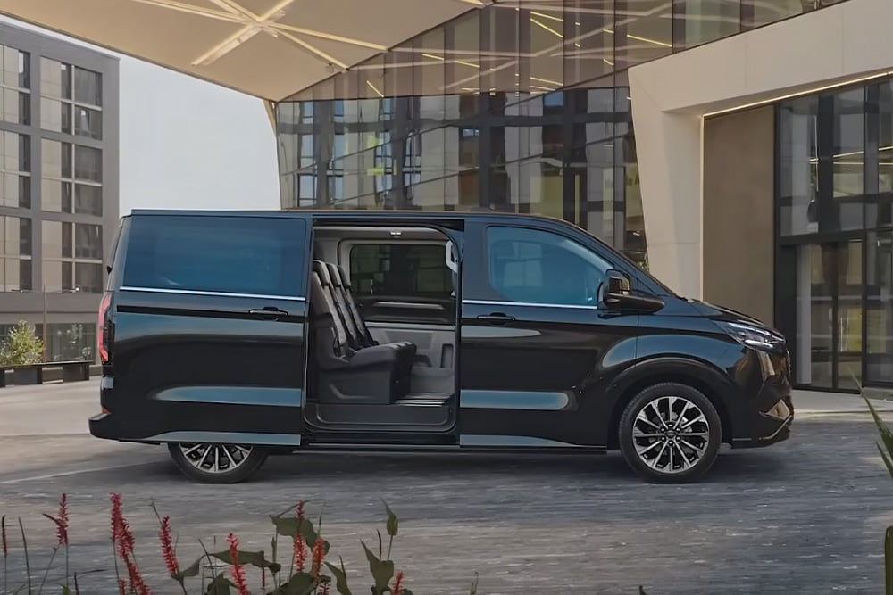 A black Ford E-Tourneo Custom is parked with its side door open, revealing the interior seating.