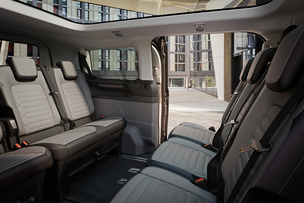 Interior view of the Ford Tourneo Custom, showing multiple rows of grey passenger seats and panoramic sunroof.