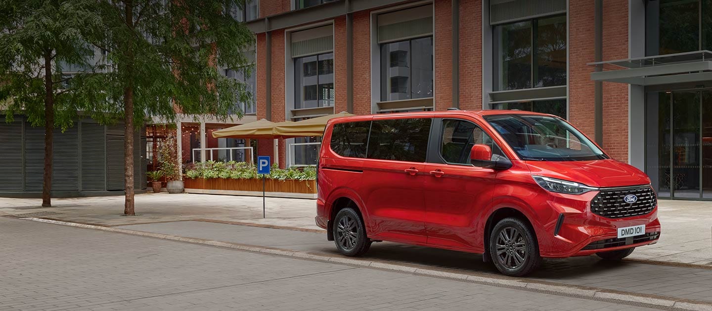A red Ford Tourneo Custom is parked on a city street. 