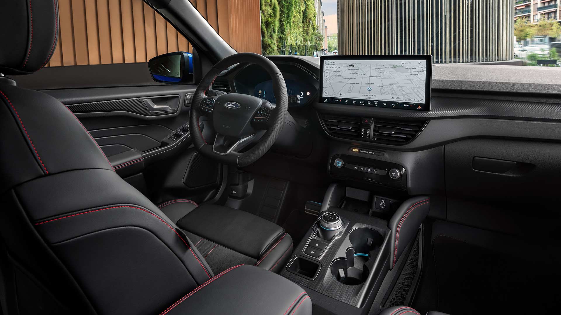Ford Kuga interior showing the Ford logo steering wheel, large SYNC® 4 touchscreen, and black seats with red stiching.