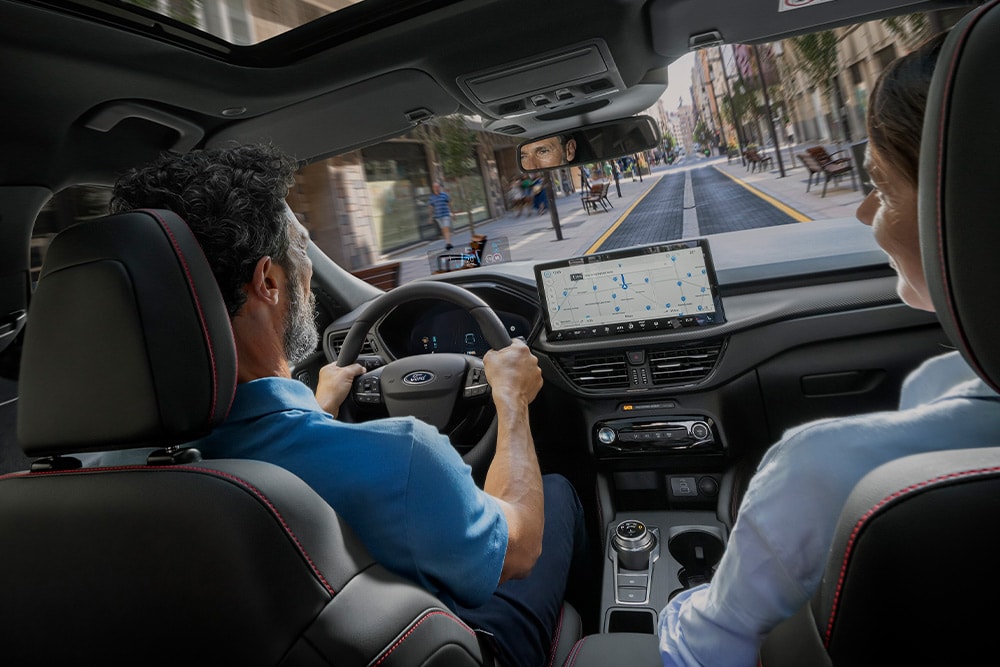 Two people in a  Ford Kuga driving along a city street using directions on the 12.3” digital display.