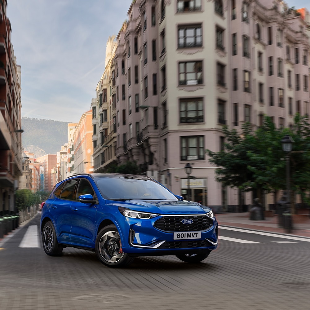 Blue Ford Kuga driving down a tree-lined city street.
