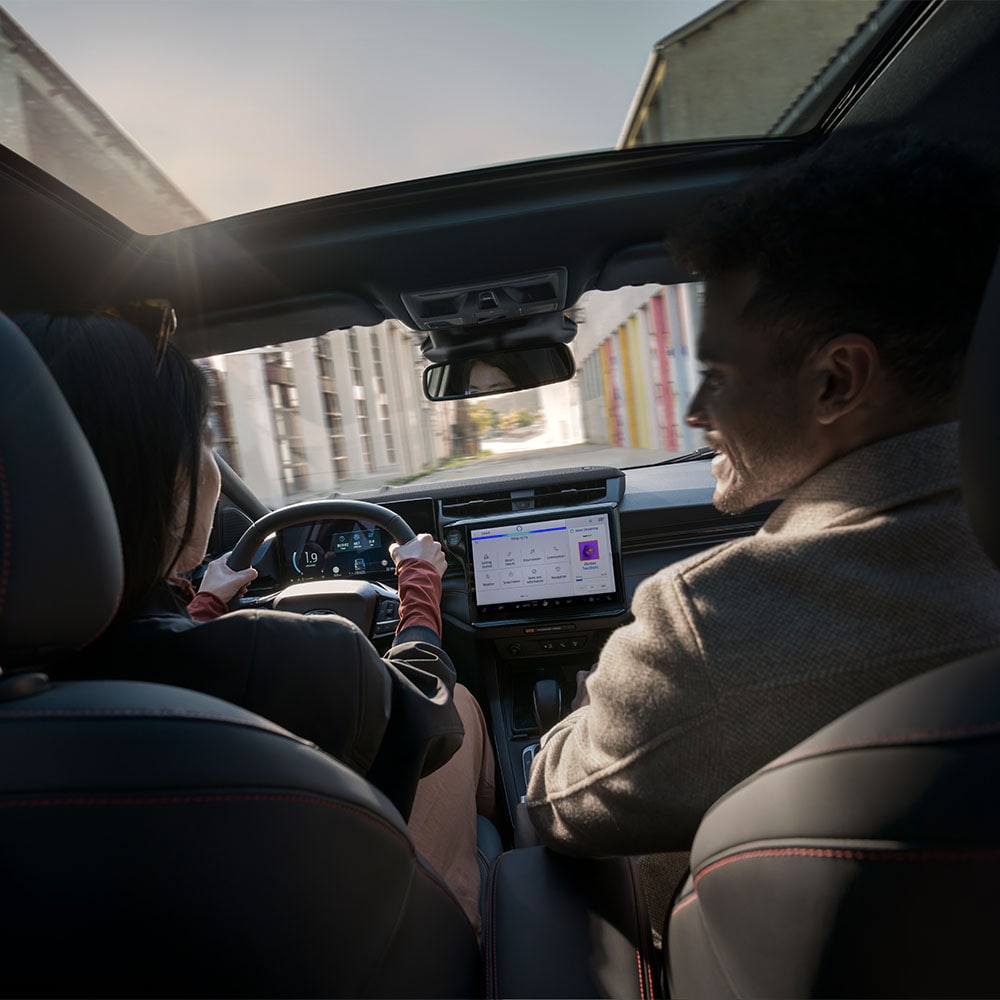 Driver and passenger chatting while driving through a sunny residential landscape.