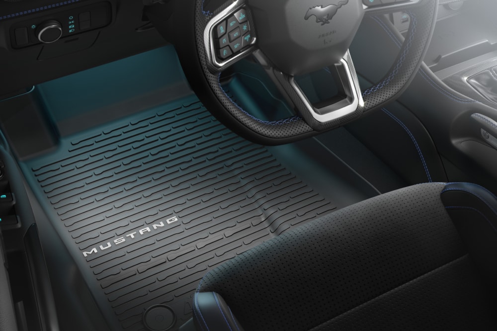 Interior view of a Ford Mustang showing the steering wheel and an all-weather floor mat with “MUSTANG” branding.