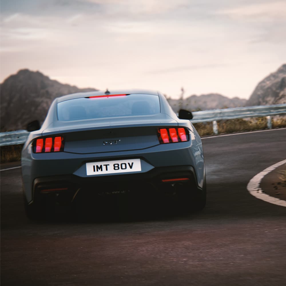 The rear of a Ford Mustang GT Fastback in Vapor Blue paint driving around a corner.