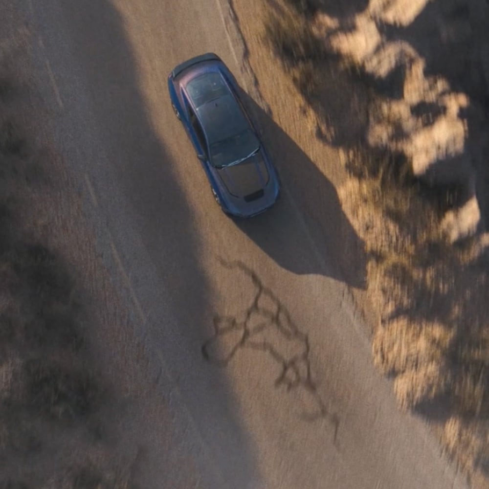 An overhead photo of a Ford Mustang Dark Horse Fastback in Blue Ember paint driving along a mountain road.