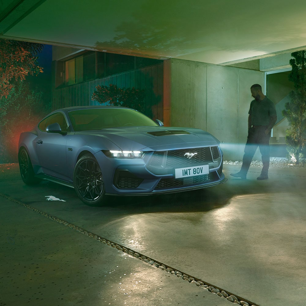 Man approaching a parked Ford Mustang with headlights illuminated, showing the car’s approach detection welcome lighting.