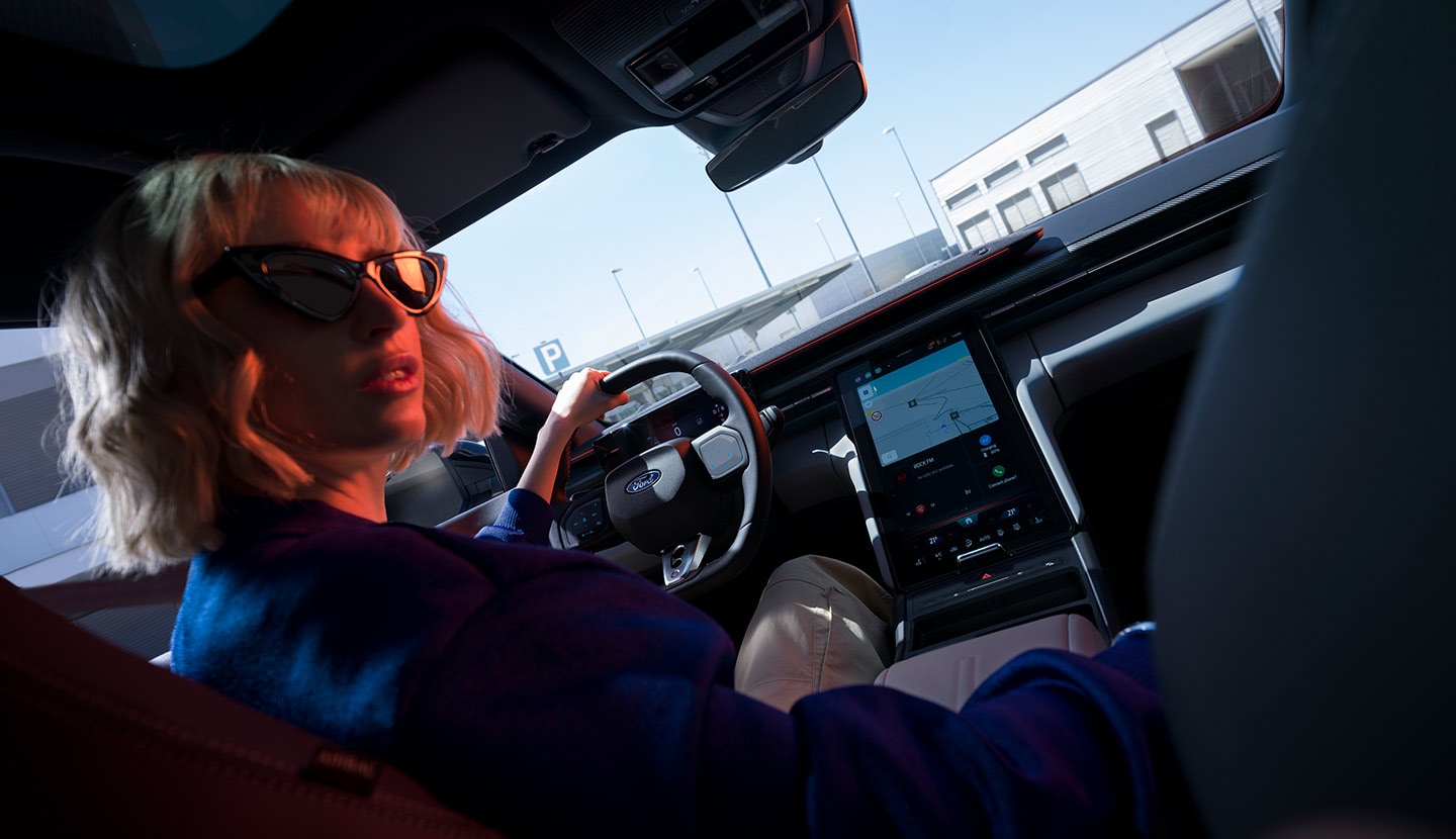 A woman sits behind the wheel of a parked Ford Capri, with the steering wheel, dashboard, and large SYNC® Move touchscreen visible.