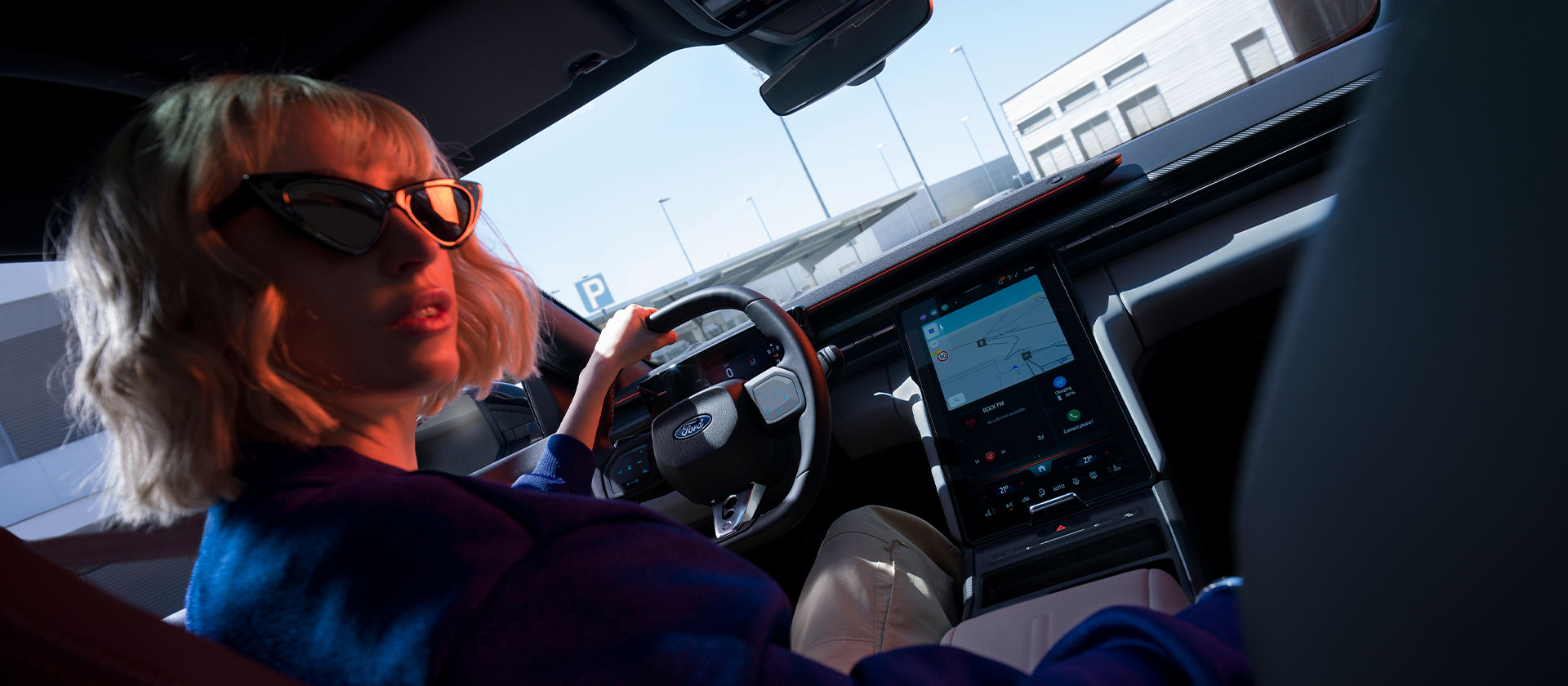 A woman sits behind the wheel of a parked Ford Capri®, with the steering wheel, dashboard, and large SYNC® Move touchscreen visible.