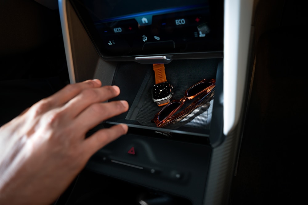 A hand reaches toward the open My Private Locker compartment in the Ford Capri®, revealing a watch and a pair of sunglasses inside.