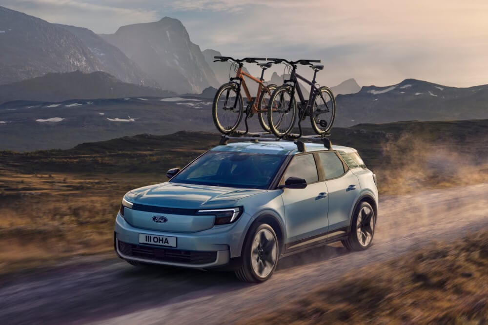 Blue Ford Explorer driving on a dirt road, with crossbars, a roof bike carrier and two bicycles mounted on the roof.