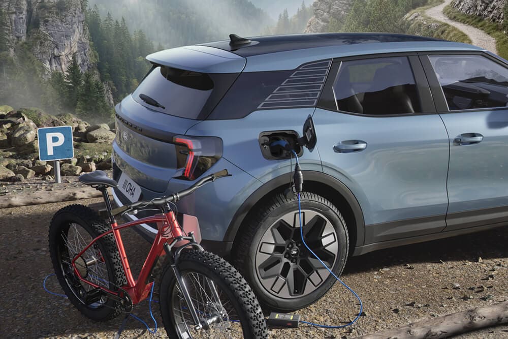 An e-bike charging from a Ford Explorer®, mountainous landscape in the background.