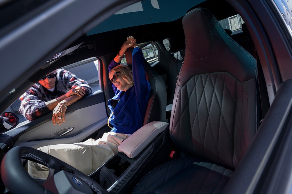 Close-up of the 12-way adjustable sport seats in a Ford Capri®. A woman sits in the passenger seat, and a man leans against the open window. The seats have integrated headrests.